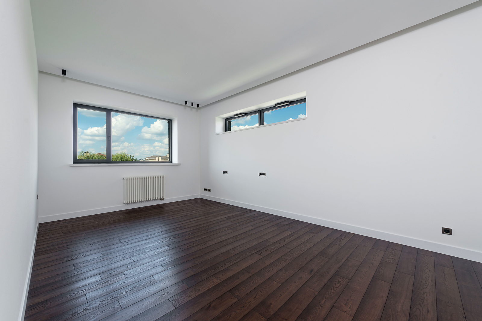 Woonkamer met een pas gelegde donkere houten vloer en daglicht uit een raamstrook